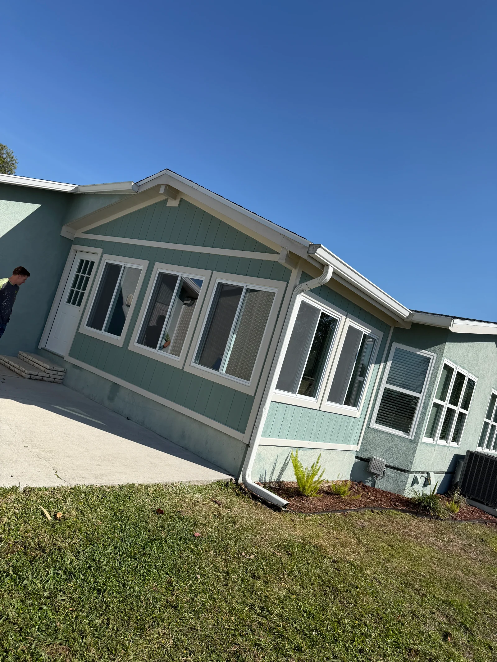 Sage green exterior repaint with cream trim, fascia, and window frames on vertical board siding and stucco