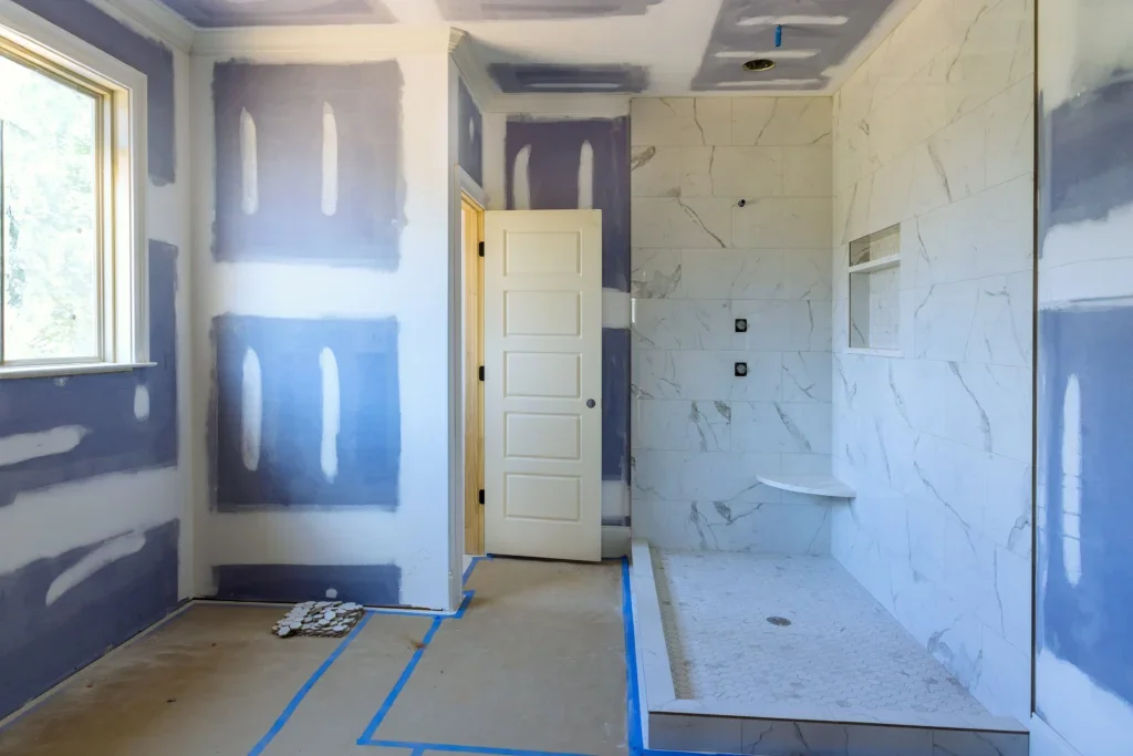 Bathroom under renovation with patched drywall, marble-look wall tile, recessed shower niche, and mosaic shower floor