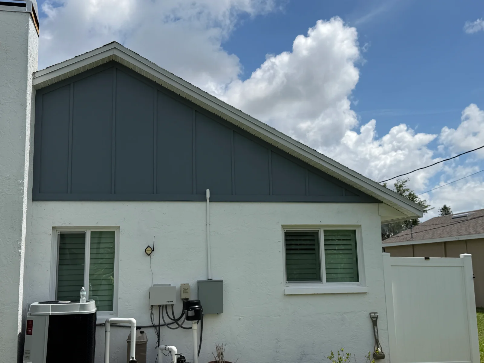 Single-story stucco home with dark blue board-and-batten gable, white trim, and dark green window shutters