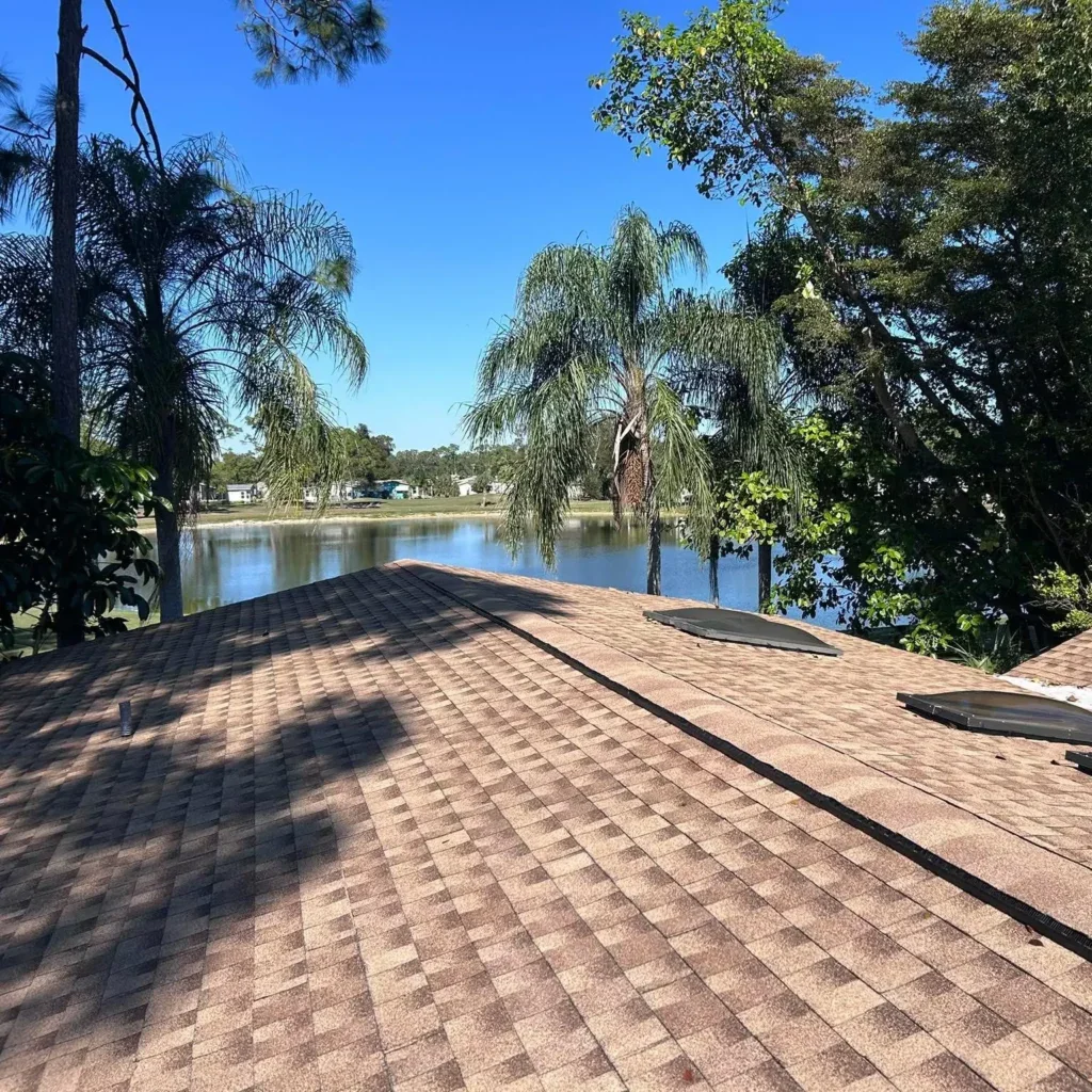 Brown dimensional asphalt shingle roof with black ridge cap and roof vents, with palm trees and lake in background